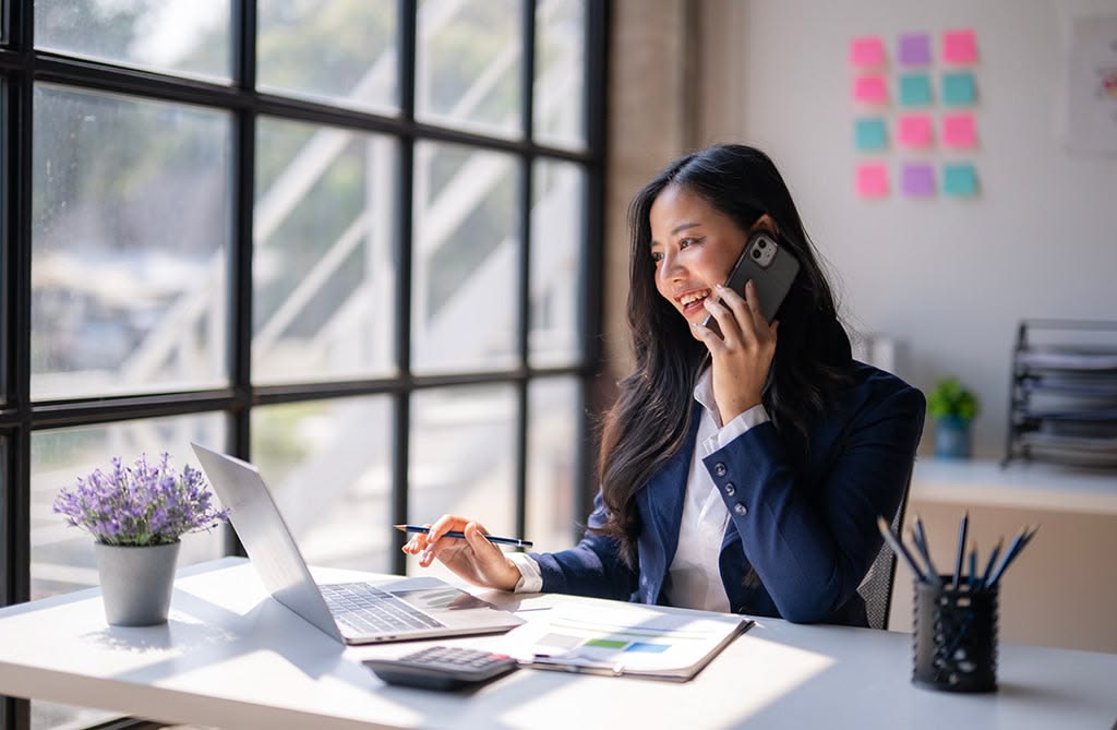 An executive smiling while a virtual assistant manages a cluttered digital calendar, email inbox, and travel itinerary on multiple screens, showing seamless organization.